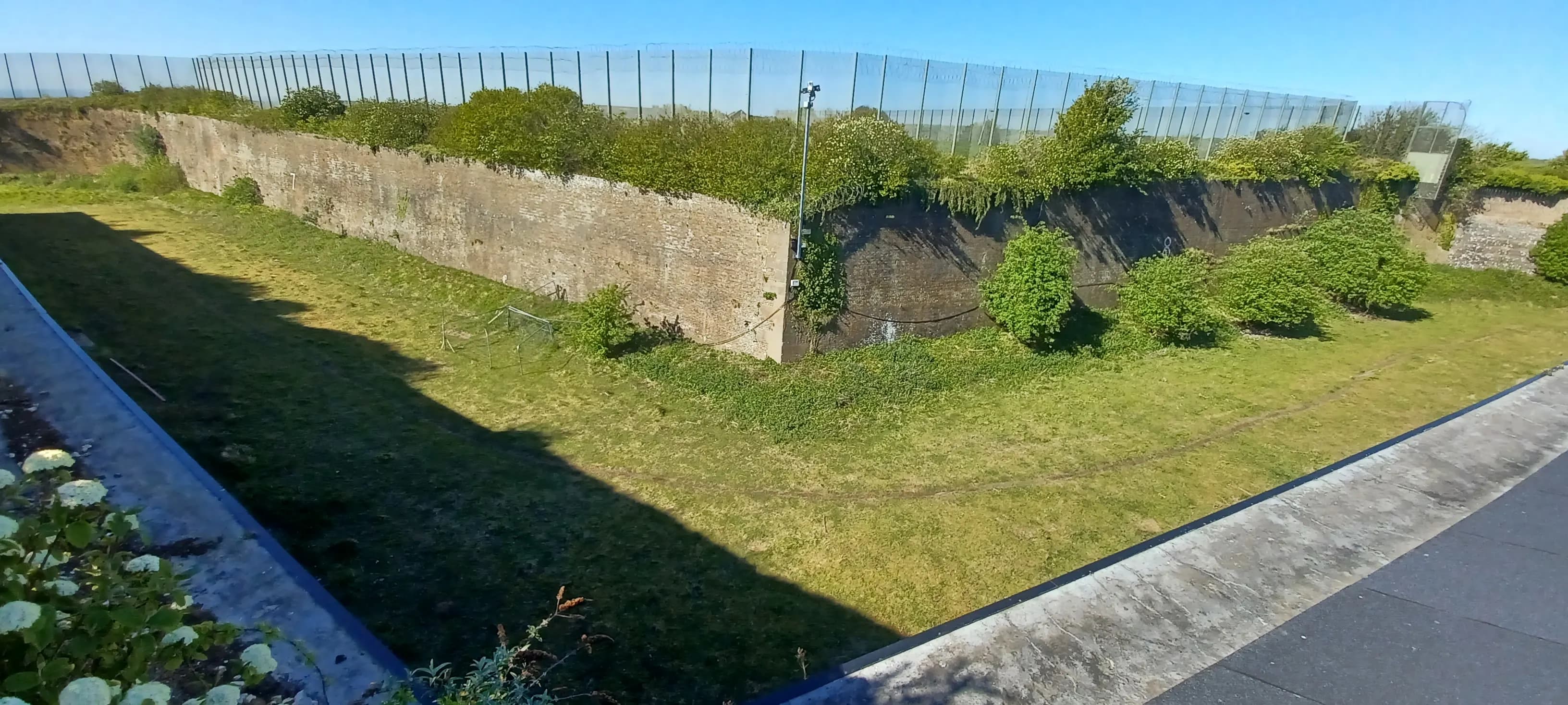 Napoleonic stone ramparts and dry moat with modern perimeter mesh fencing