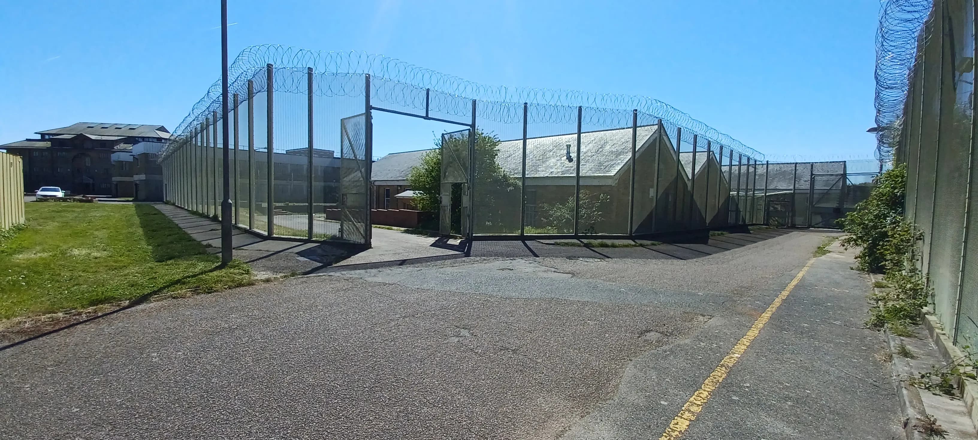 Open mesh security gate with concertina wire and compound buildings beyond