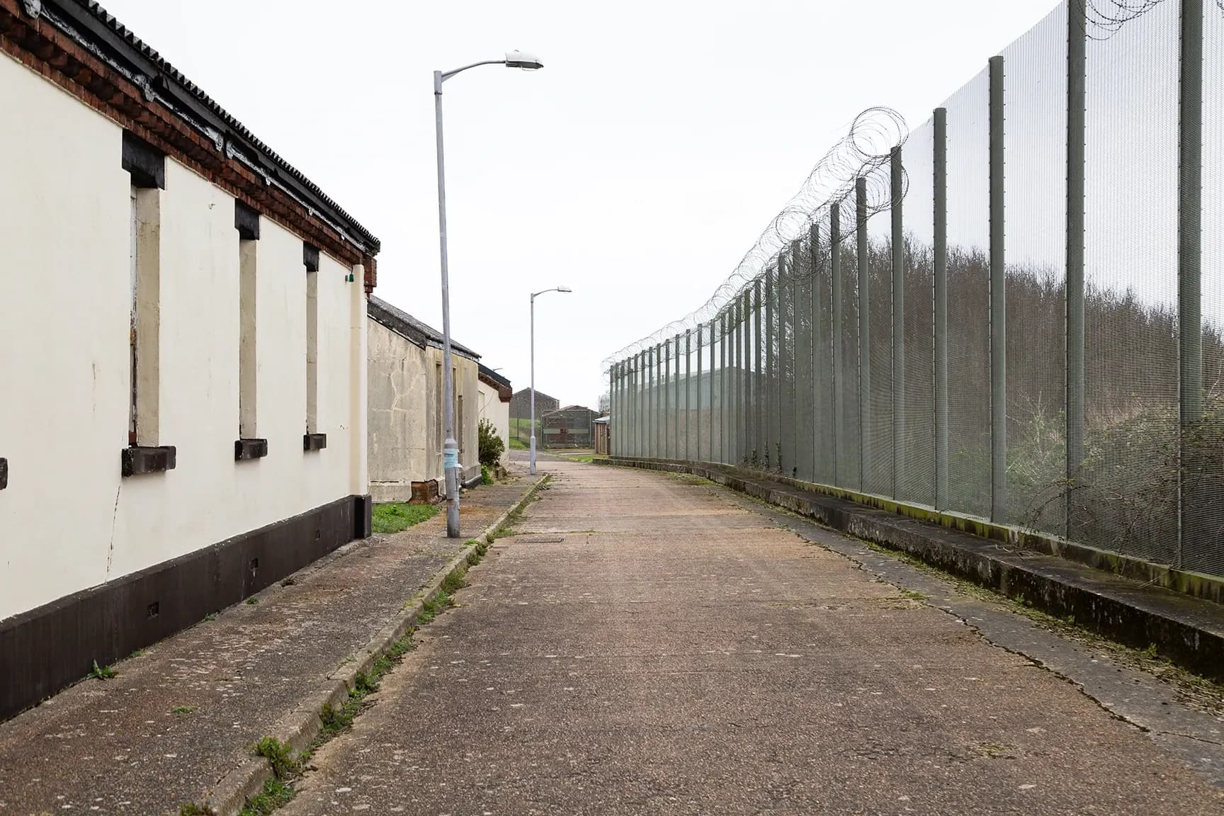 Internal asphalt road through the compound toward a razor-wire security gate between brick buildings