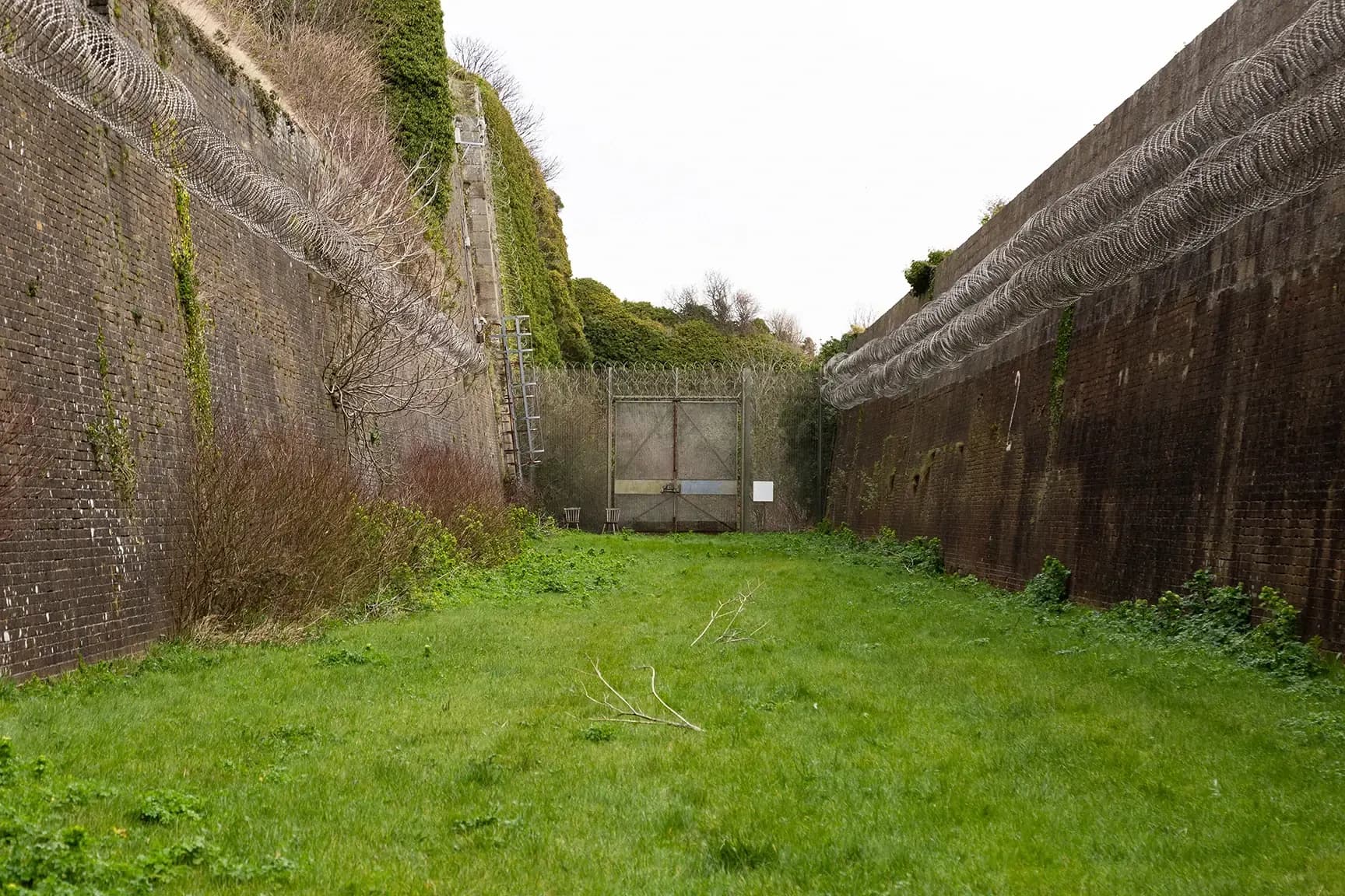 Secure perimeter fence and gate with razor wire, asphalt access route and grassy embankments