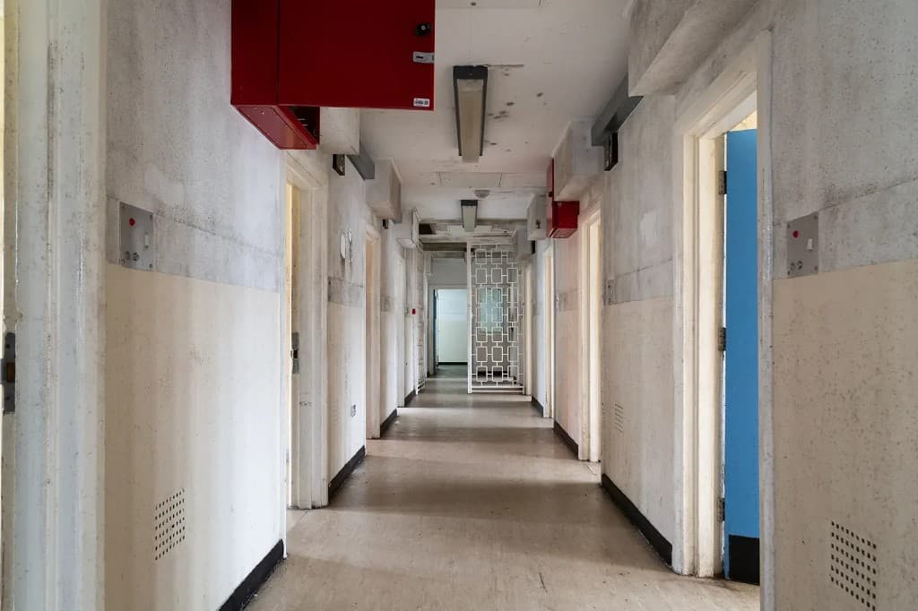 Institutional custodial corridor with doorways, overhead lighting and worn linoleum flooring