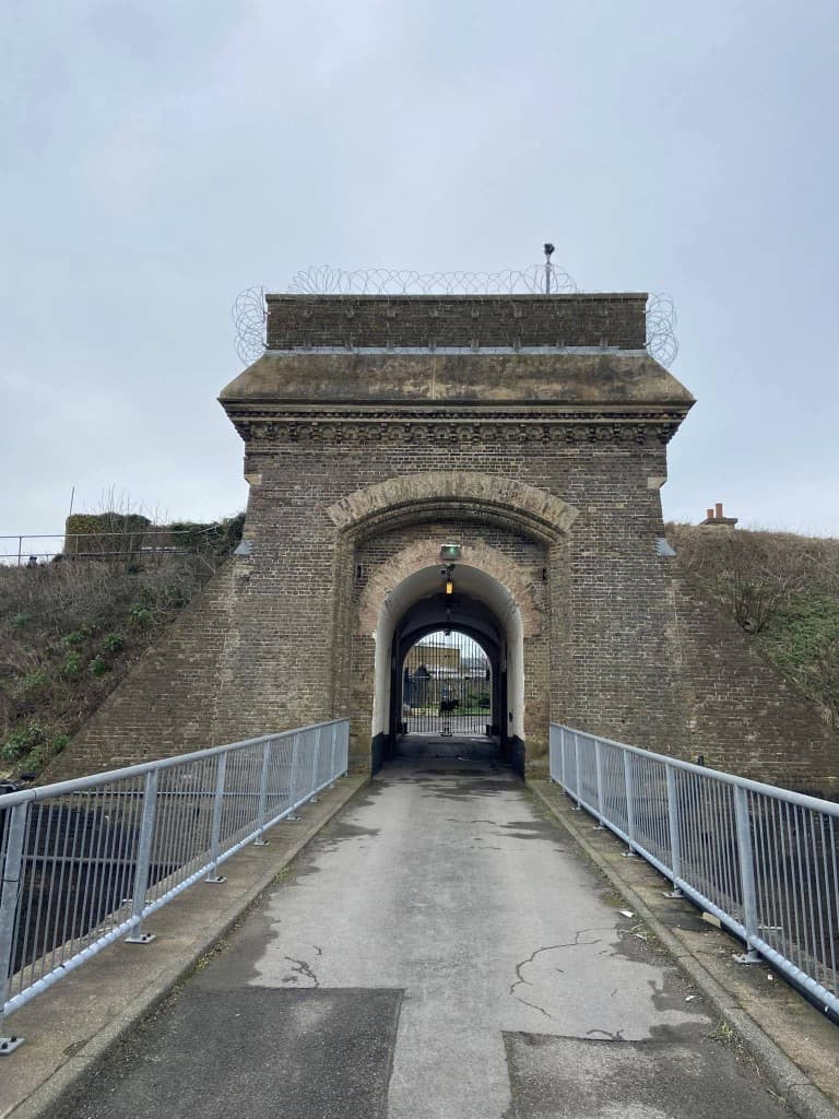 Historic brick gatehouse entrance with paved bridge and razor wire