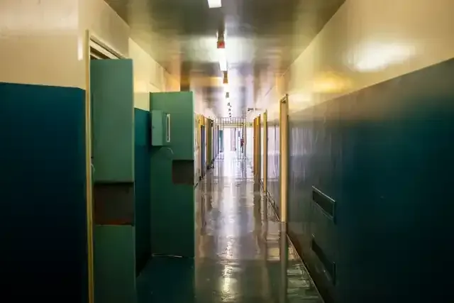 Segregation unit corridor with teal doors, glossy flooring and barred gate at the far end